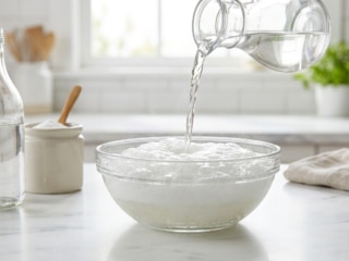 Du vinaigre blanc est versé sur du bicarbonate de soude dans un bol en verre, créant une réaction effervescente.