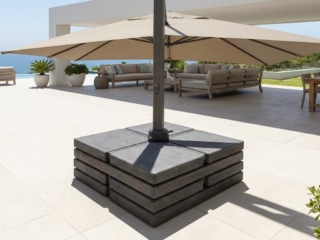 Pied de parasol déporté massif composé de dalles en béton superposées sur une terrasse ensoleillée.